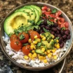 Overhead view of a burrito bowl with sliced avocado, black beans, corn, cherry tomatoes, white rice, and fresh cilantro garnish in a round metal bowl.