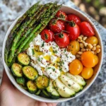 Close-up of a spring vegetable bowl with roasted asparagus, zucchini, cherry tomatoes in various colors, and whipped feta cheese drizzled with olive oil.