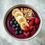 Berry Bliss Smoothie Bowl topped with sliced banana, fresh blueberries, raspberries, and granola in a white ceramic bowl.