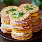 Stacked Ritz cracker party sandwiches with layers of ham, cheese, and cream cheese topped with green onion garnish on a brown plate.