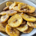 Close-up of thinly sliced banana chips with cinnamon seasoning and visible salt crystals in a white bowl