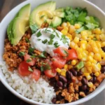 Turkey taco burrito bowl with white rice, seasoned ground turkey, black beans, corn, cherry tomatoes, avocado, sour cream, and fresh cilantro garnish