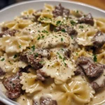 Creamy Beef and Bowtie Pasta with Alfredo Sauce in a white bowl with browned beef chunks and fresh parsley garnish