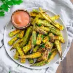 Crispy air fryer okra served on white speckled plate with orange dipping sauce and fresh parsley garnish