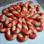 Freshly baked candy cane cookies with red and white twisted stripes cooling on paper towels after baking