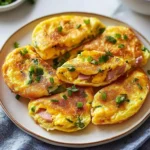 Golden mini breakfast omelets filled with diced ham, cheese, and green onions served on a beige plate.