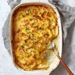 Freshly baked scalloped potatoes in a white ceramic dish with golden cheese crust and fresh herb garnish.