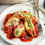 Single serving of Christmas stuffed shells on plate with fork, showing melted cheese and herb garnish
