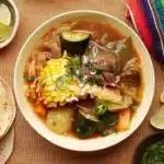 Overhead view of Caldo de Res Mexican beef soup with lime wedges and tortillas ready for serving