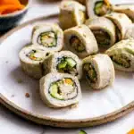 Beautifully arranged sushi sandwich rolls on a white plate showing colorful fillings of cucumber, carrot, avocado and chicken
