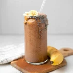 Mocha protein coffee smoothie on wooden serving board with whole banana and cocoa powder dusting