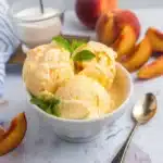 Peach ice cream dessert with fresh peach slices and mint garnish in ceramic bowl