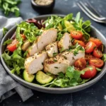Juicy herb-seasoned chicken breast slices on a bed of fresh greens with cherry tomatoes and cucumbers in a gray bowl
