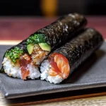 Two temaki sushi hand rolls on a slate plate featuring salmon, tuna, avocado, and green onions with visible rice and crisp nori wrapping.