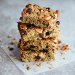 Stack of homemade protein breakfast bars with nuts, seeds, and dried fruit on parchment paper