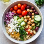 Colorful Quinoa Mediterranean Bowl featuring tri-color quinoa, cherry tomatoes, cucumber, red onion, chickpeas, Kalamata olives, and crumbled feta cheese with olive oil visible on the side.