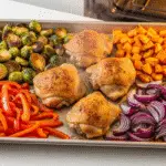 Sheet pan dinners with roasted chicken thighs Brussels sprouts sweet potatoes on rimmed baking sheet