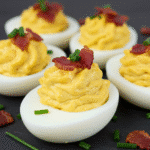 Honey bacon cheddar deviled eggs garnished with crispy bacon bits and fresh chives on white serving platter
